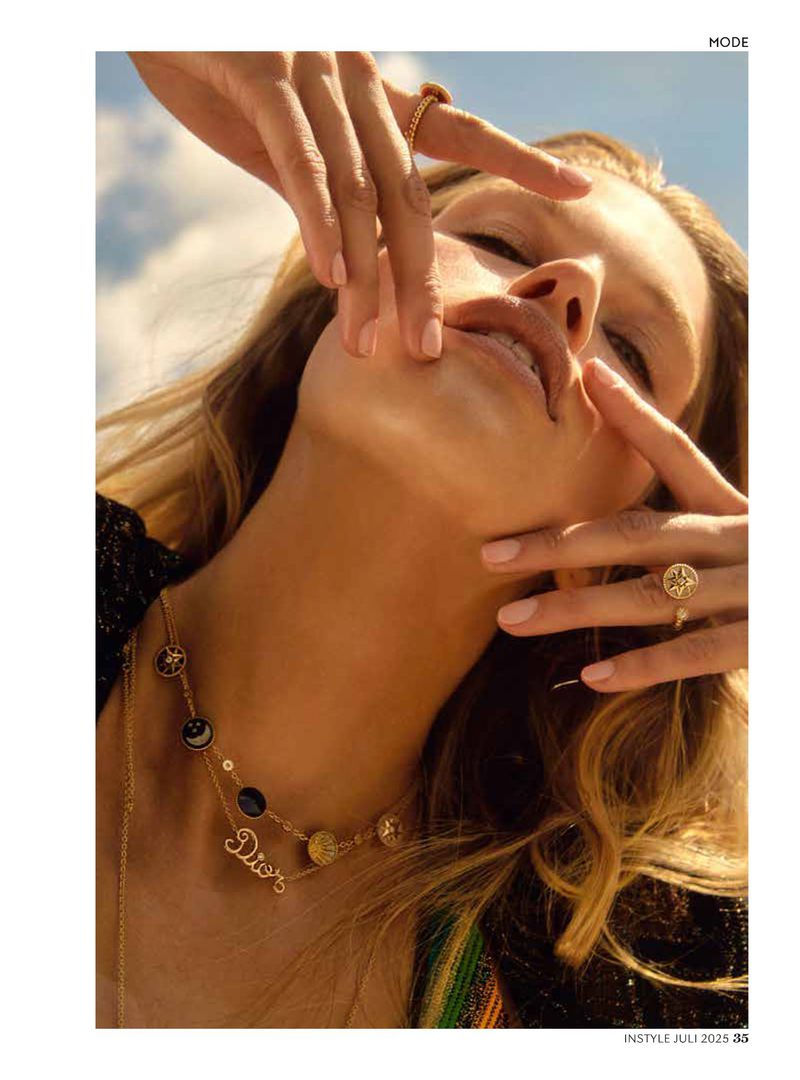 Close-up fashion shot of a fair-skinned woman outdoors with blond hair, wearing jewelry, against a sky background, looking up and posing.