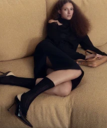 Model reclining on a textured gold sofa wearing a black dress and slingback heels with a tan leather bag