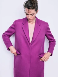 Model wearing a vibrant magenta tailored wool coat against a plain white studio background.