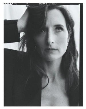 Portrait of Grace Gummer with dark hair running her hand through her hair, wearing a dark blazer against a white backdrop.