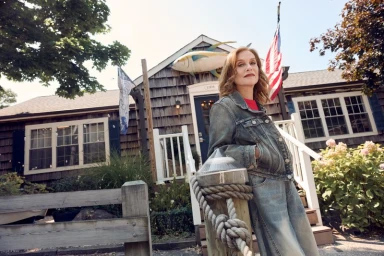 Isabelle Huppert wearing a denim jacket standing outdoors near a shingle house for Paris Match