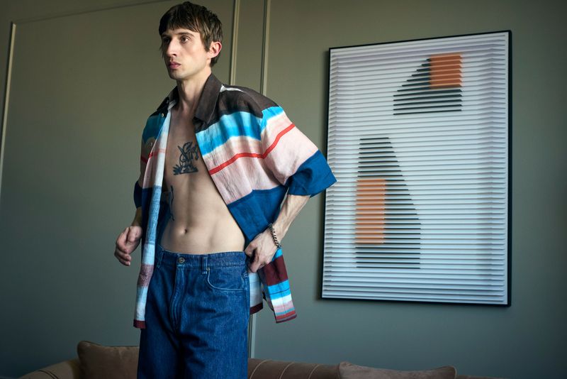 Model Jakop Weissbarth wearing an open striped shirt and blue jeans in an interior room for Zoo Magazine.