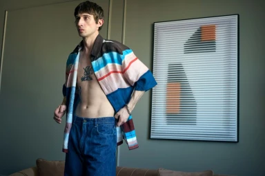 Model Jakop Weissbarth wearing an open striped shirt and blue jeans in an interior room for Zoo Magazine.