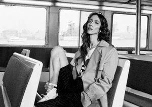 Model Alana Zimmer seated on a ferry bench wearing a trench coat and patterned shorts in a black and white editorial photograph.