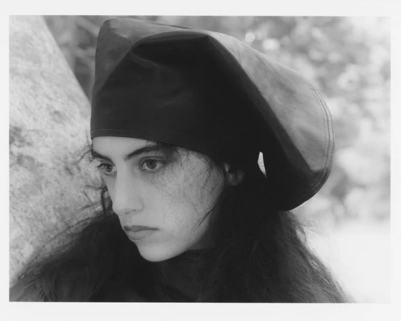 Portrait of a woman wearing a dark fitted beret and dark clothing outdoors against a light stone surface.