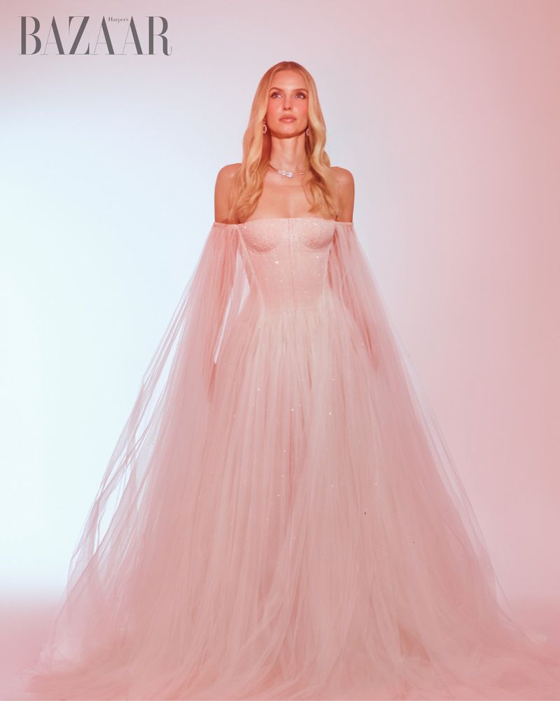 Leonie Hanne in a pink off-shoulder tulle gown with sheer sleeves standing against a warm gradient background