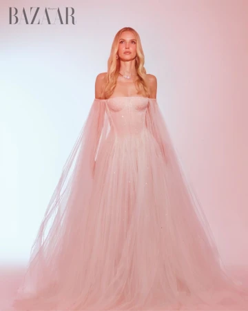 Leonie Hanne in a pink off-shoulder tulle gown with sheer sleeves standing against a warm gradient background