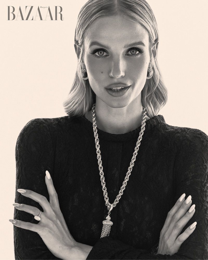 Portrait of blonde woman wearing textured black top with rope necklace and earrings against plain background