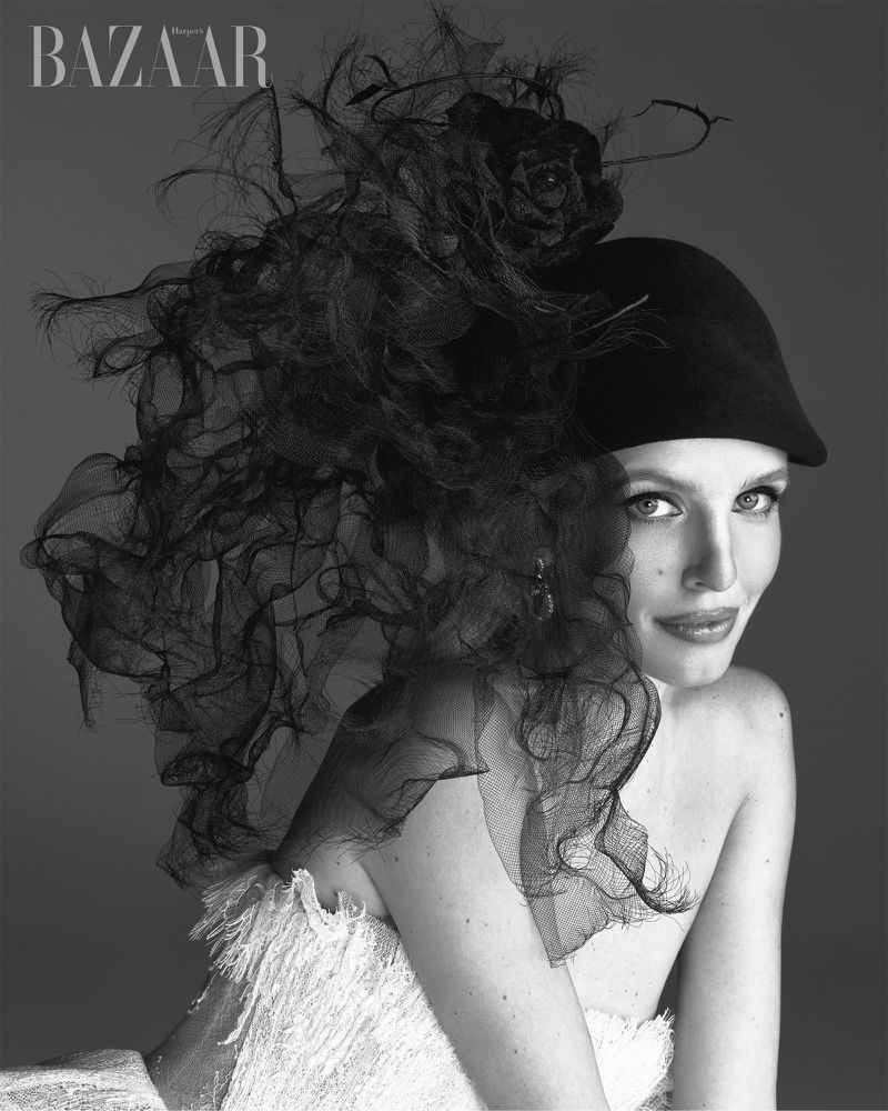 Leonie Hanne in Harper's Bazaar Vietnam editorial wearing a black feathered hat and white textured gown against a grey background.