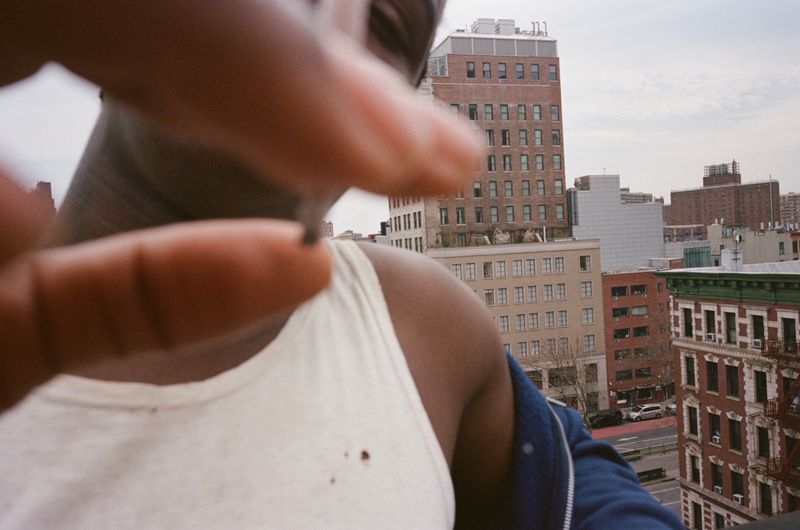 Close-up portrait of Daniel Caesar wearing a white tank top against an urban rooftop backdrop for Interlope Magazine