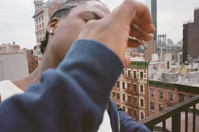 Man wearing a blue zip-up hoodie standing on a rooftop overlooking city buildings