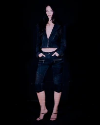 Model wearing dark denim jacket and matching pants standing against a black background for Mark Fast S/S 27