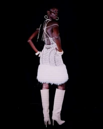 Model in white halter dress with feathered hem and knee-high boots against a black seamless background
