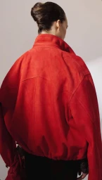Back view of a model wearing a bright red suede jacket with an upright collar against a neutral studio backdrop