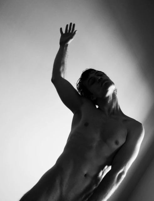 Monochrome portrait of a shirtless adult male, arm raised, against a bright background with light rays creating a striking contrast.