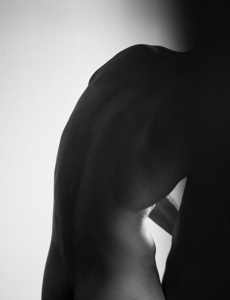 Monochromatic studio shot of an adult male torso showcasing muscular definition and form against a gradient white to black backdrop, emphasizing anatomy.
