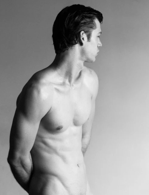 Monochrome portrait of a nude adult male with muscular build, looking off to the side against a plain light grey background in a studio.