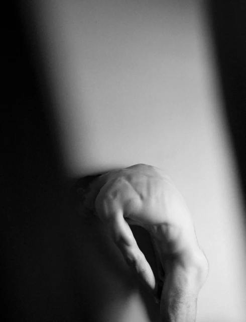 Monochrome shot of a person's hand pressing against a surface, creating a subtle indentation and dramatic contrast between light and shadow.