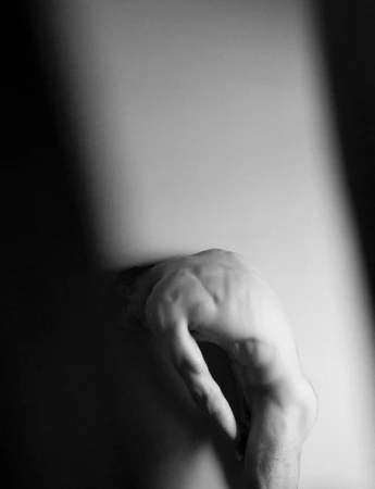 Monochrome shot of a person's hand pressing against a surface, creating a subtle indentation and dramatic contrast between light and shadow.