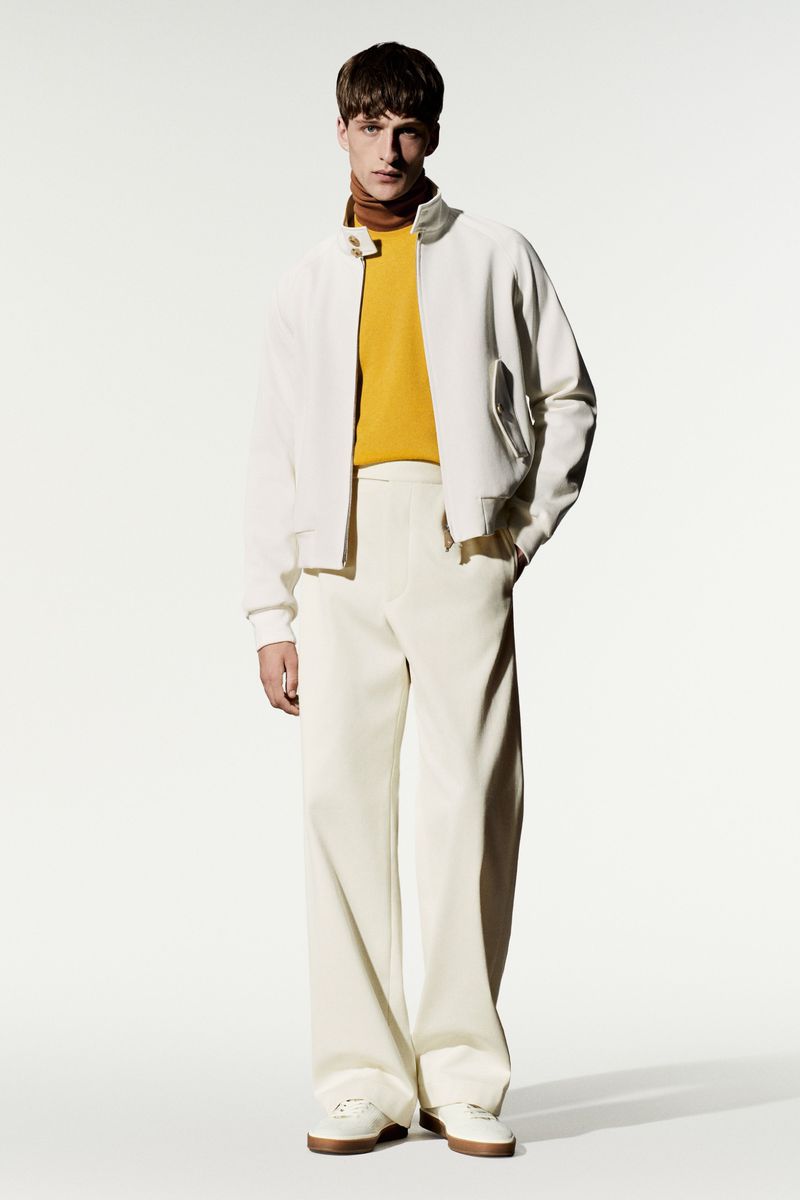 Model wearing a white jacket, yellow shirt, and white trousers against a plain white studio backdrop.