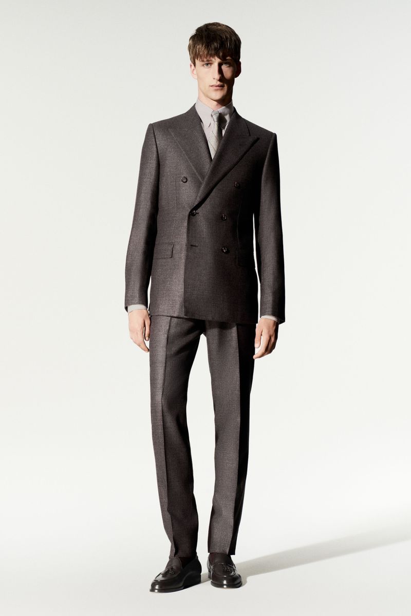 Full-length portrait of a male model wearing a grey double-breasted suit against a plain white background for Loro Piana.