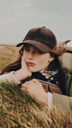 Model wearing a brown cap and green outerwear lying in grassy landscape for Max Mara campaign