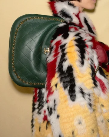 Model wearing vibrant multi-colored fur coat carrying a large quilted green leather handbag for Heroine Magazine