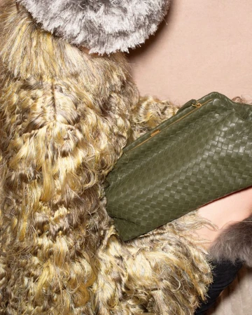 Close-up of a textured shaggy coat and an olive green woven leather clutch bag against a plain background.