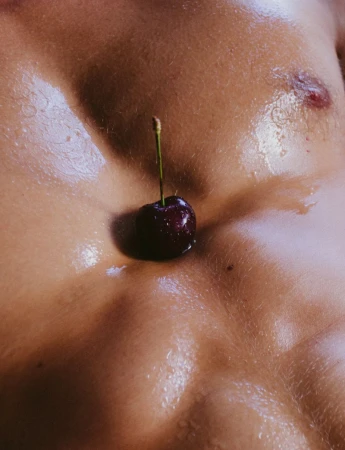 Close-up of a single cherry on an adult male's chest, highlighting the contrast between the fruit's deep red and the skin's texture.