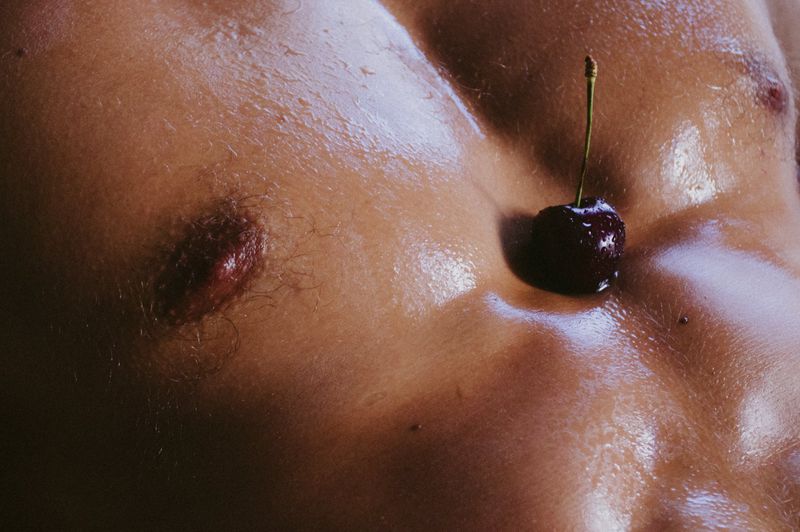 Close-up shot of a man's torso with a single cherry resting on his chest, emphasizing the skin's texture and the cherry's contrast.