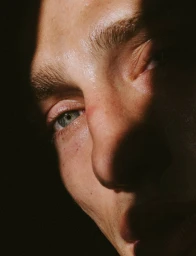 Extreme close-up portrait of a man face with dramatic directional lighting highlighting his eye and nose bridge.