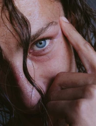 Close-up portrait of a person with wet hair framing their face and a finger touching their temple