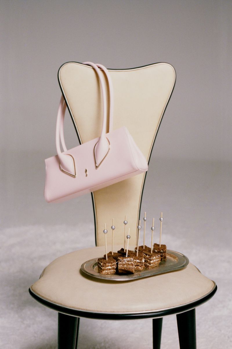 A pastel pink handbag hanging from a cream-colored chair holding a silver tray with bite-sized layered cakes on toothpicks.