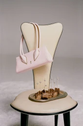 A pastel pink handbag hanging from a cream-colored chair holding a silver tray with bite-sized layered cakes on toothpicks.