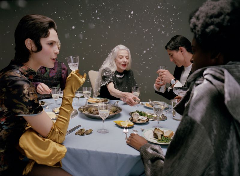 Group of people seated around a dining table set with food and glassware under falling snow for Mixte