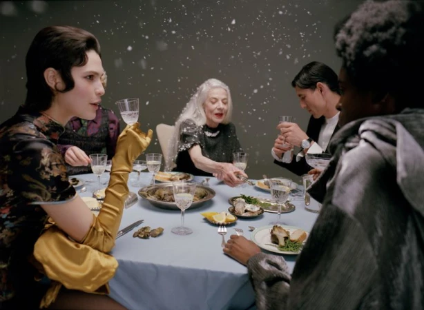 Group of people seated around a dining table set with food and glassware under falling snow for Mixte