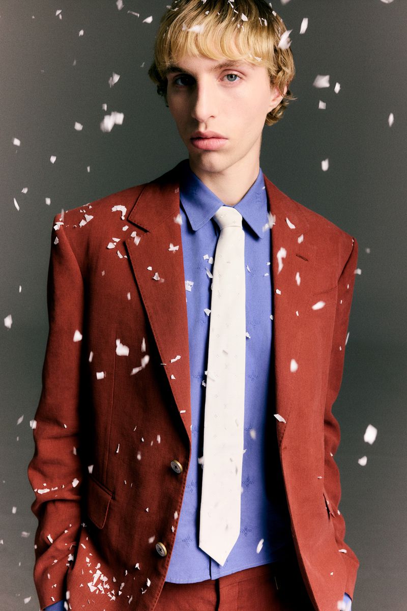 Model in rust-brown suit jacket with a blue shirt and white tie amid falling snow or confetti flakes