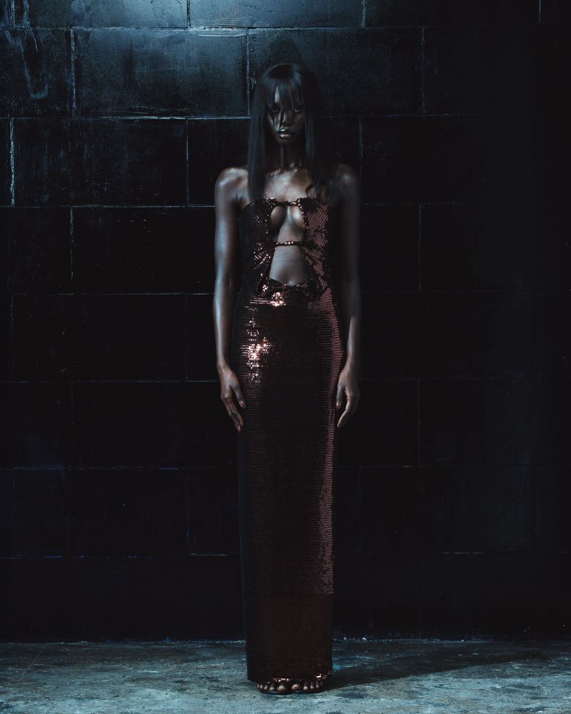 Model standing against dark tiled wall wearing a strapless metallic sequined gown by Mowalola for The Hunger S/S 27 Lookbook.