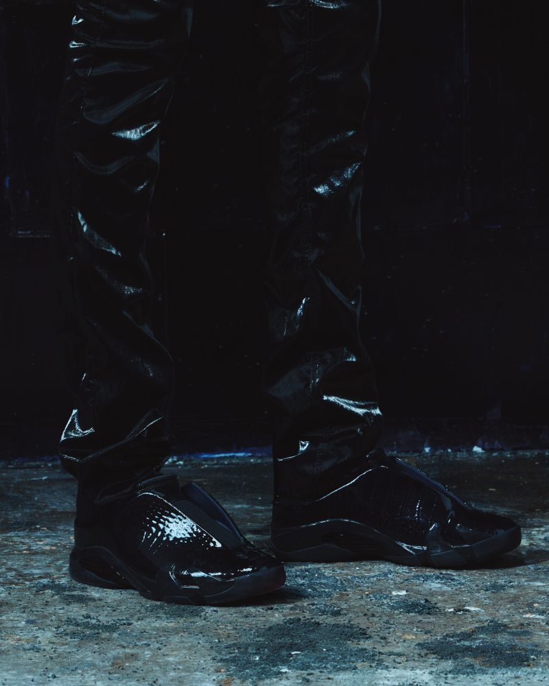 Close-up of shiny black sneakers and glossy black trousers against a dark textured ground