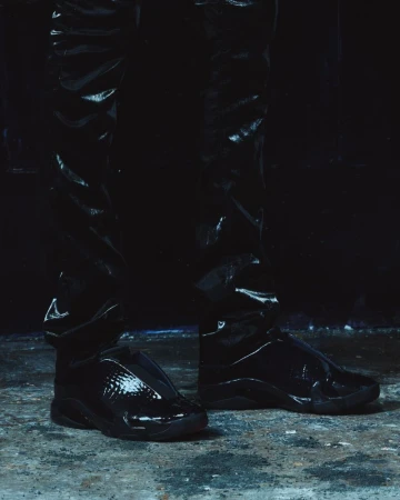 Close-up of shiny black sneakers and glossy black trousers against a dark textured ground
