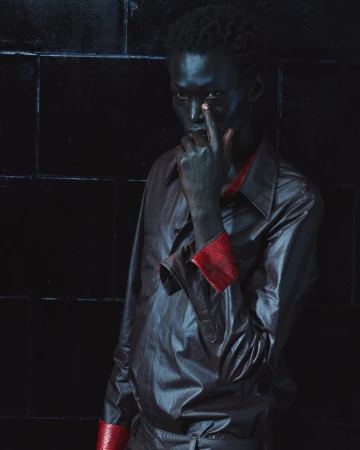 Portrait of a black man wearing a dark shirt with red cuffs posing against a black tiled wall