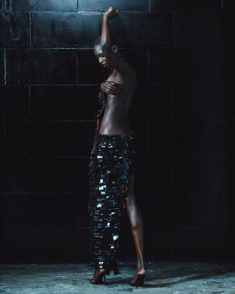 Model in a dark textured skirt posing against a dark tiled wall for Mowalola The Hunger lookbook