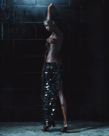 Model in a dark textured skirt posing against a dark tiled wall for Mowalola The Hunger lookbook