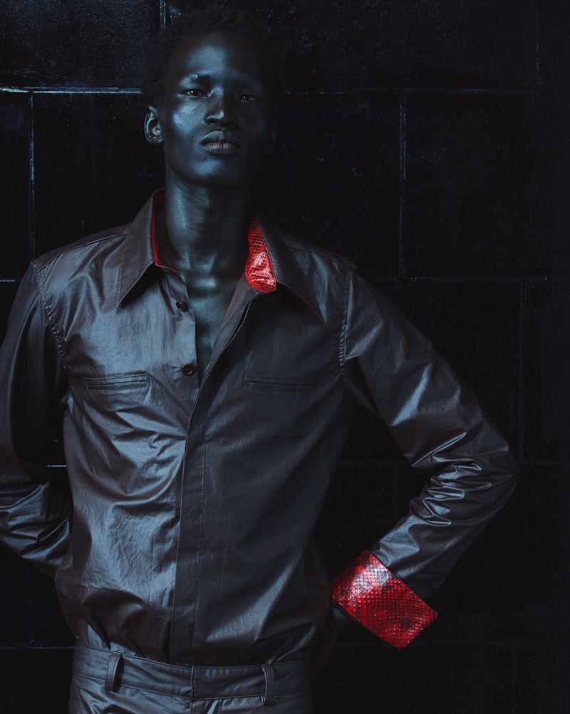 Portrait of a black man wearing a dark shirt with red cuffs against a dark textured background for Mowalola