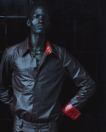 Portrait of a black man wearing a dark shirt with red cuffs against a dark textured background for Mowalola