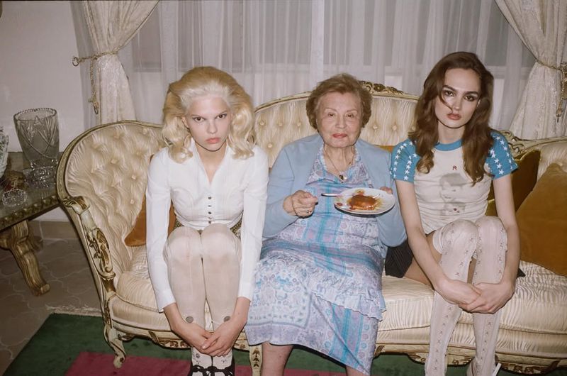 Three women seated on a vintage cream sofa holding a small plate, photographed by Terry Richardson for Enfants Riches Deprimes.