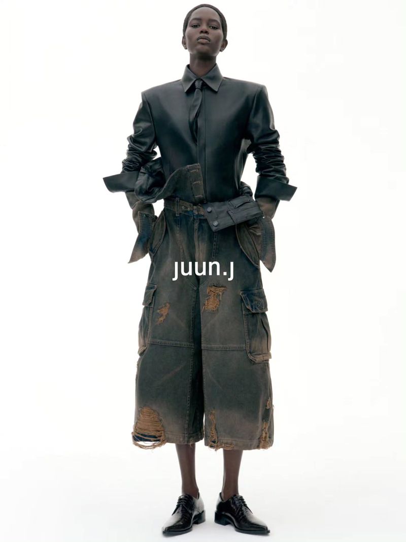 Model wearing dark leather shirt and distressed cargo shorts against a plain white background for Juun.J S/S27.