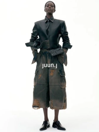Model wearing dark leather shirt and distressed cargo shorts against a plain white background for Juun.J S/S27.