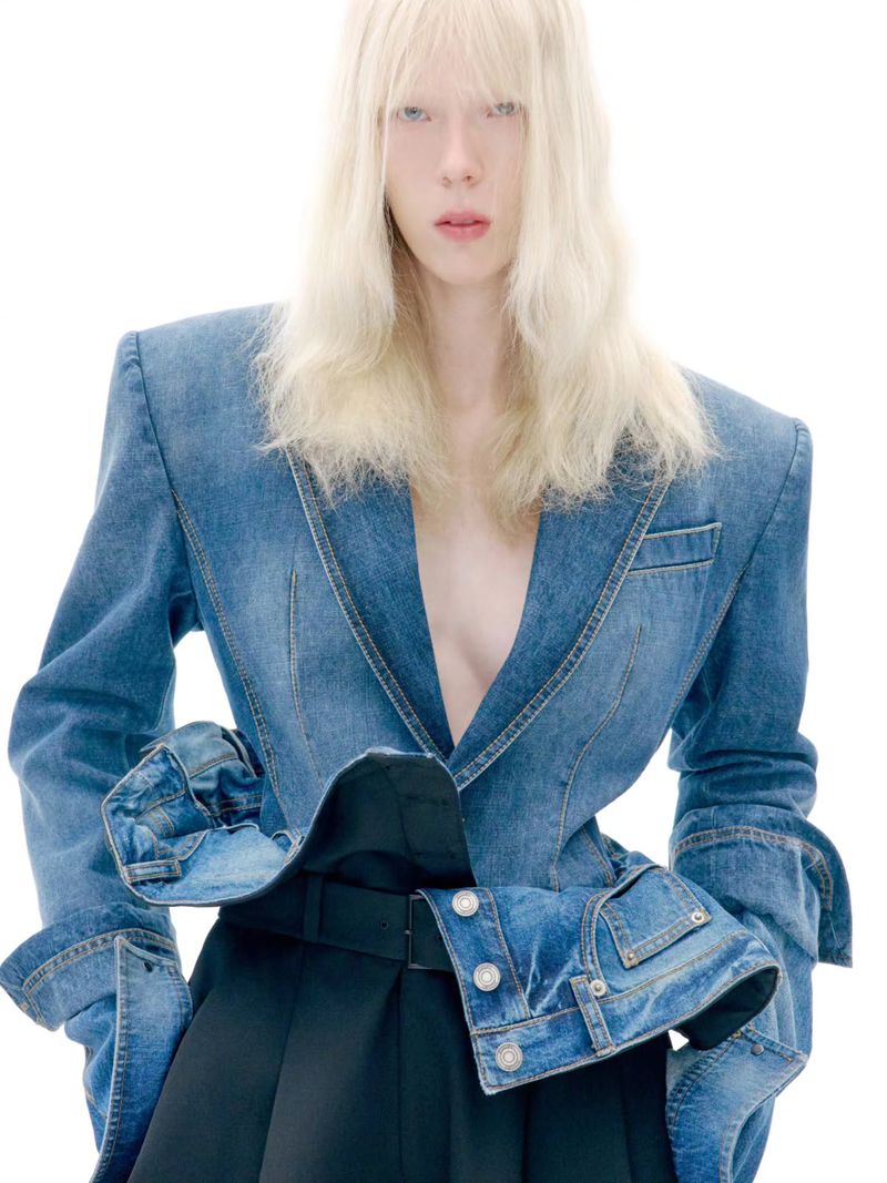 Model with long blonde hair wearing a structured denim jacket against a bright white background