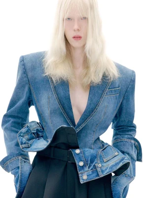 Model with long blonde hair wearing a structured denim jacket against a bright white background